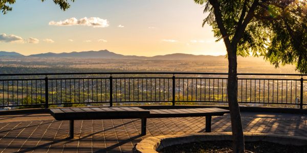 Scenic sunset view from a park bench overlooking a city and mountains.