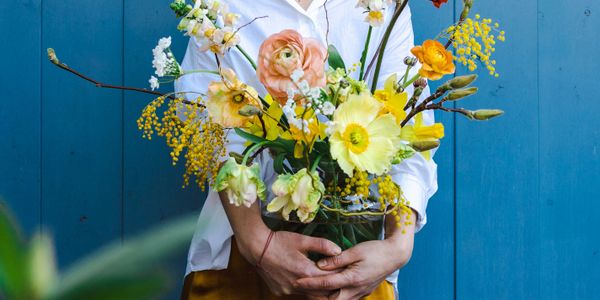 Person holding a vibrant bouquet of mixed spring flowers against a blue background.