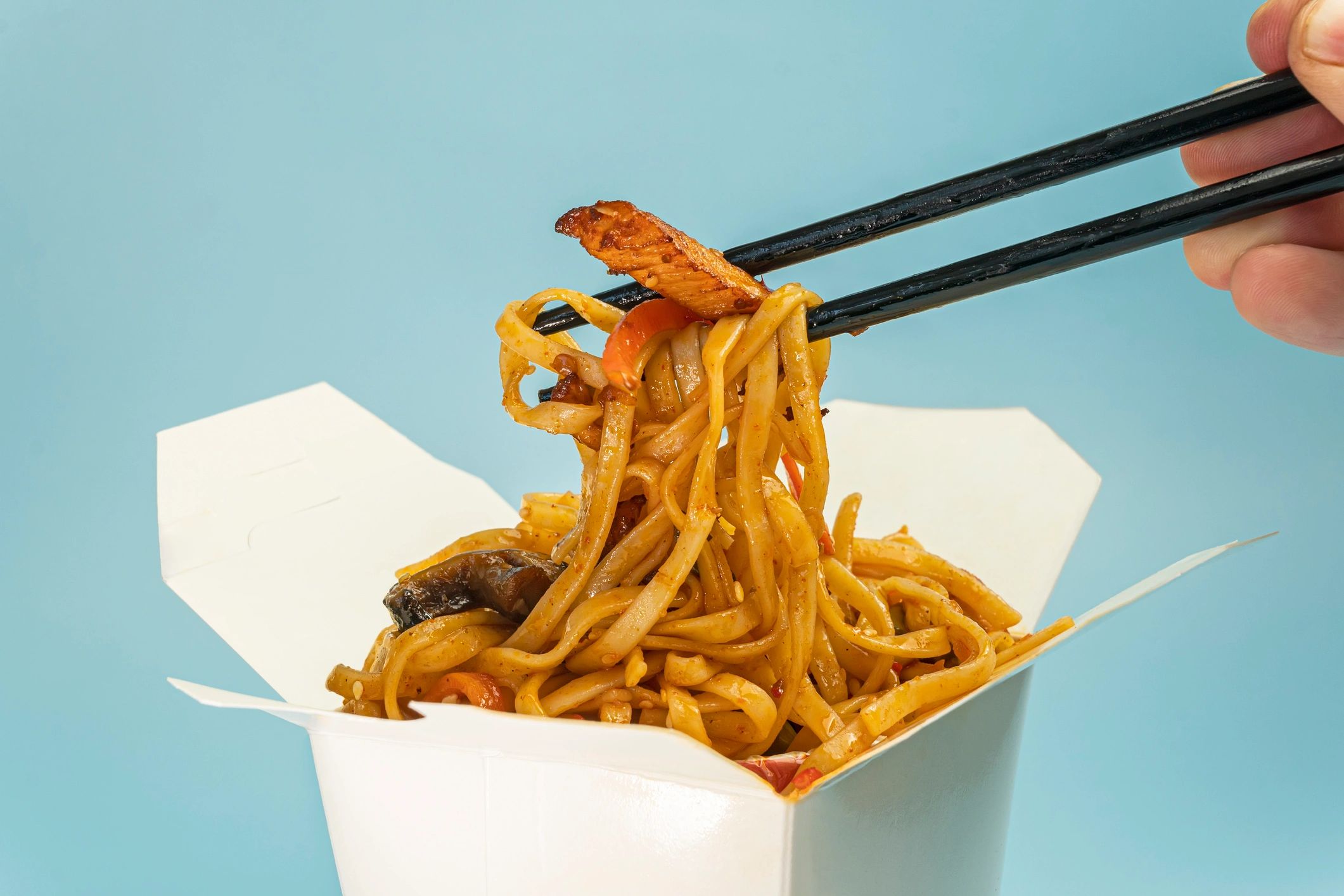 Chopsticks picking up noodles and meat from takeout box.
