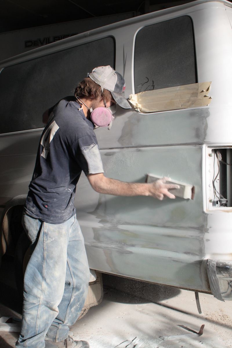 A young man does some sanding on a van that is in for body repairs.