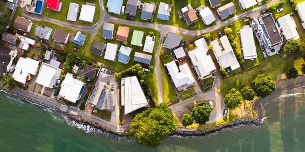 Aerial view of a coastal neighborhood with houses and green lawns by the water.