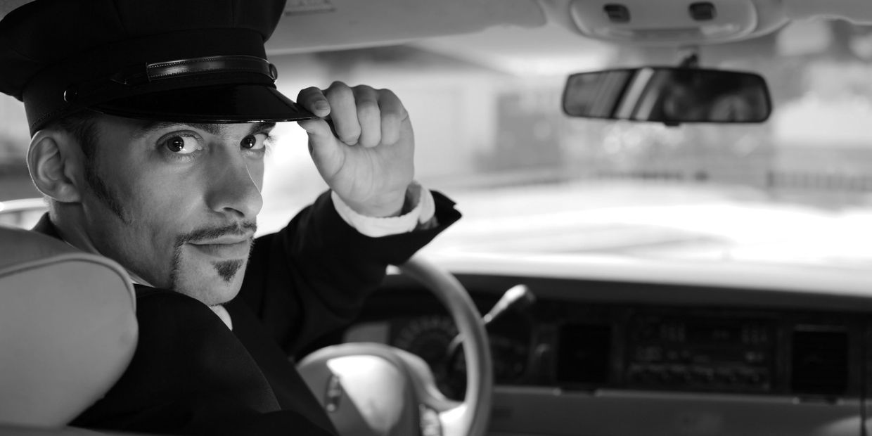 Chauffeur tipping his hat while sitting in a car.