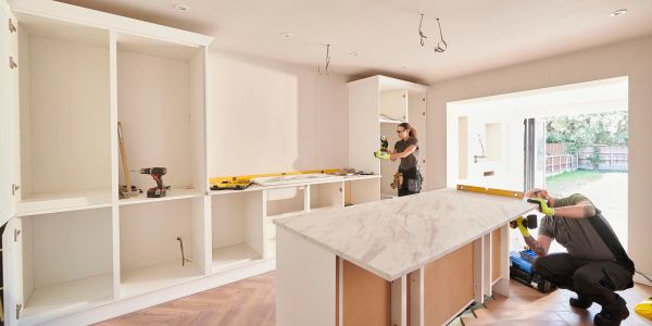 Two workers install kitchen cabinets and countertops.