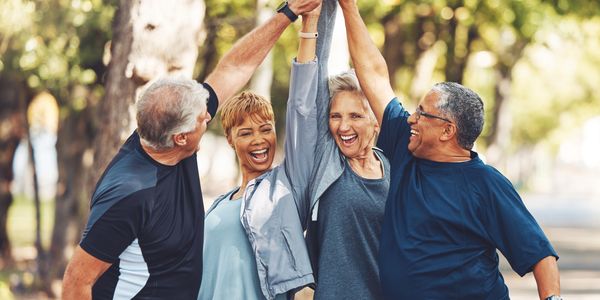 Four elderly people in a group high-five in a park.