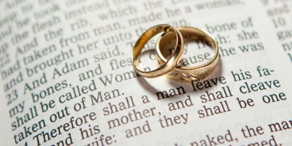 Two gold wedding rings on an open Bible page.
