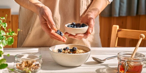 Person adding blueberries to a bowl of oatmeal.