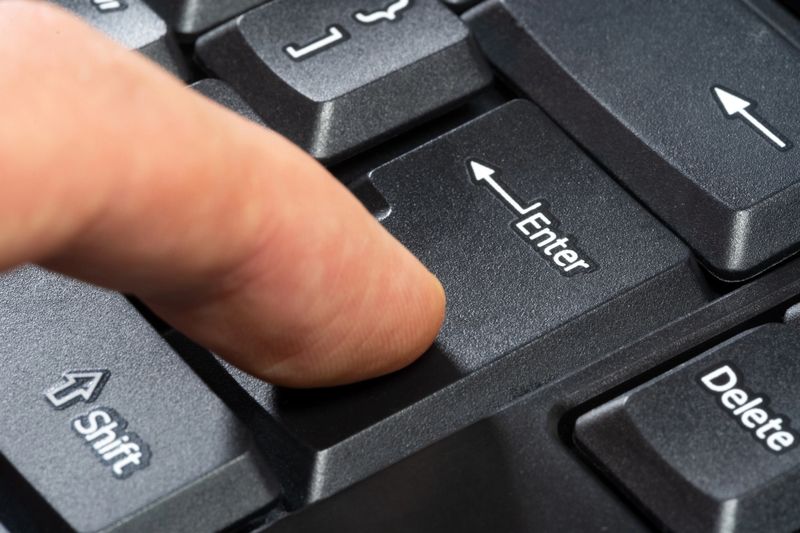 Finger pressing the enter key on a simple black computer keyboard, object macro, extreme closeup, side view. Confirmation, sending a message, chatting online abstract concept. Enter key press hand