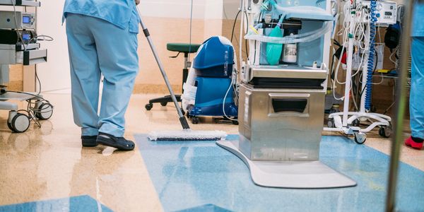 Hospital staff cleaning and mopping the floor in a medical room.