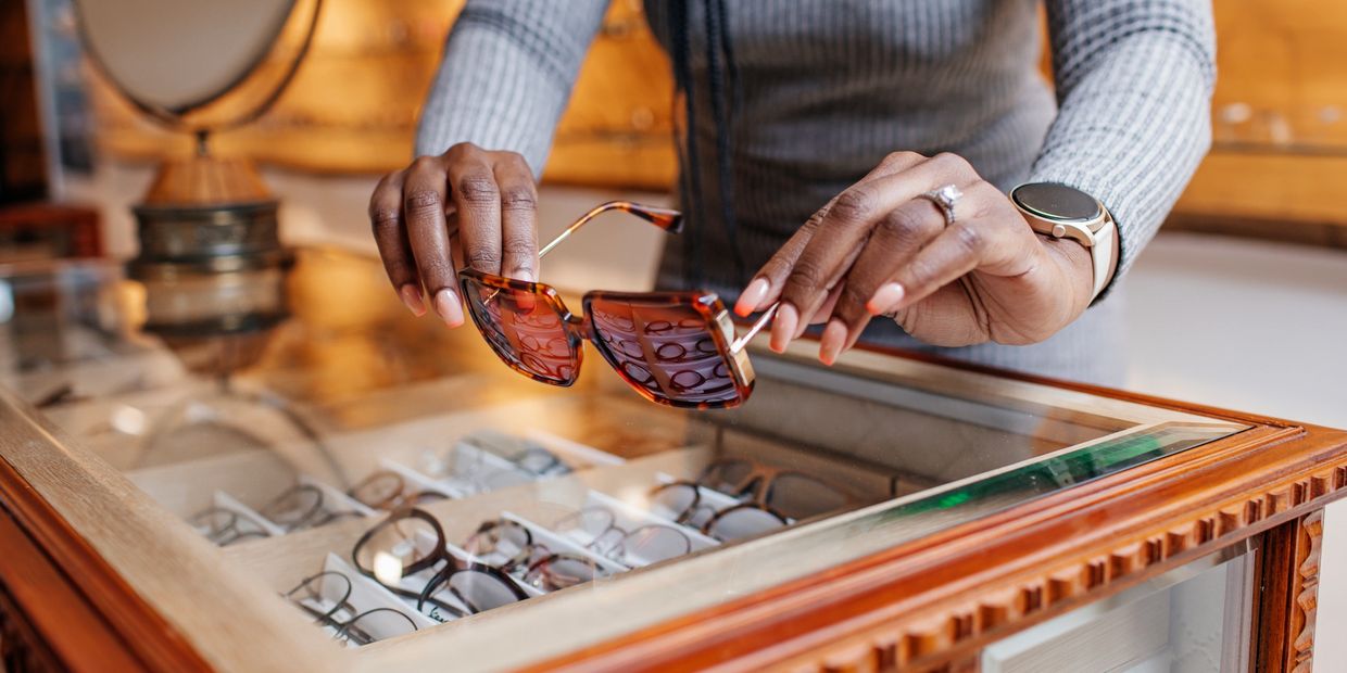 Person holding tortoiseshell sunglasses above a display case of glasses.