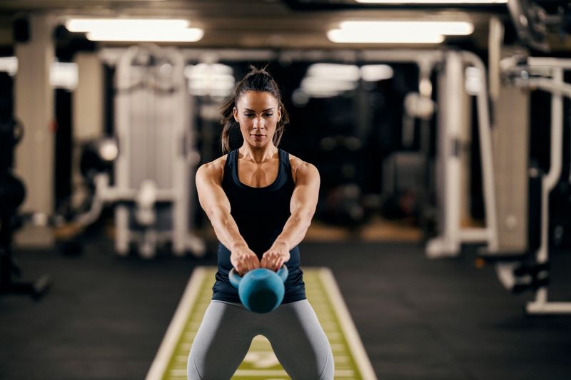 A bodybuilder in shape is swinging kettlebell while standing in a gym.