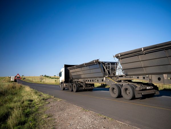 A large truck with two trailers on a rural road under a clear blue sky.