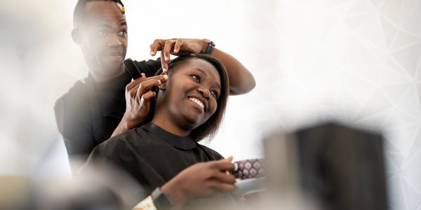 A woman smiling while getting her hair done by a hairstylist.