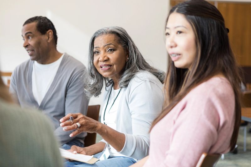 Before the start of the support group meeting, the senior adult female leader introduces herself to an unrecognizable woman.