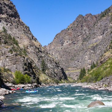 People rafting on a river in a rocky mountain canyon.