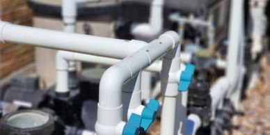 Close-up of white PVC pipes and blue valves in a plumbing system outdoors.