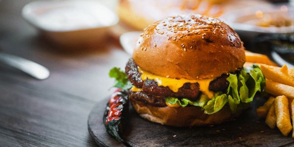 A cheeseburger with lettuce and fries on a wooden board.