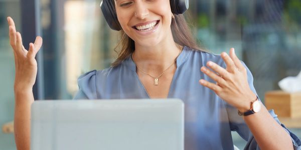 Happy woman with headphones video chatting on laptop in modern office.