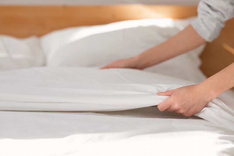 Hands of young european woman makes white bed with blanket in bedroom interior, close up, cropped, free space. Domestic chores and good morning, services work at home and hotel, order and cleanliness