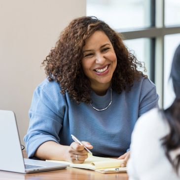 Smiling woman in blue sweater writing notes during a meeting.