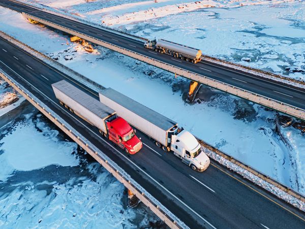 Two semi-trucks and a tanker truck travel on snowy highways and bridges.