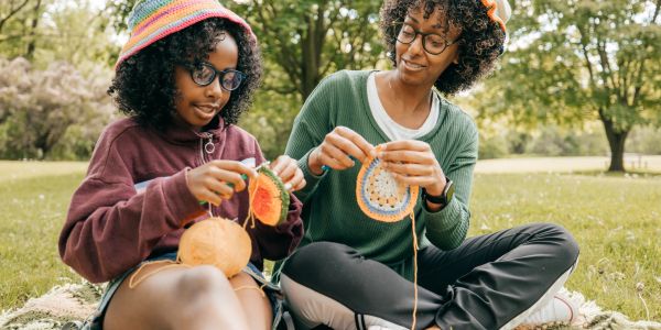 Two people crocheting outdoors on grass.