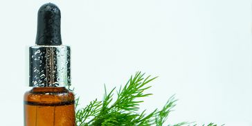 Amber dropper bottle with fresh green herbs on white background.