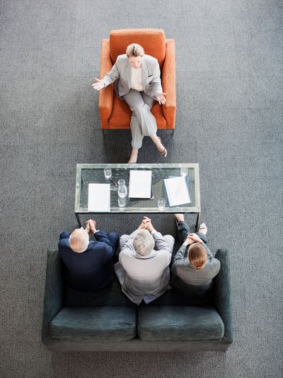 One woman talking to three seated people in a meeting.