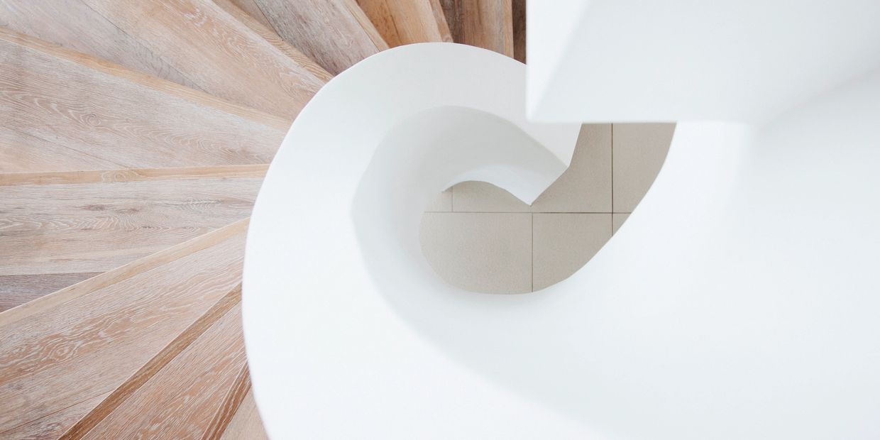 Top view of a modern spiral staircase with wooden steps and white railing.