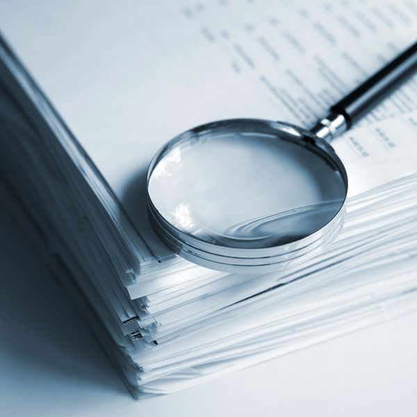 Magnifying glass resting on a thick stack of documents.