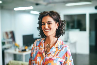 Smiling woman with curly hair in colorful shirt in a modern office.