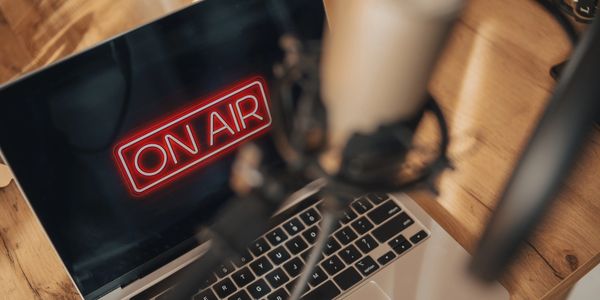 MacBook with On Air logo graphic plus podcast mic and screen blurred in front. 
