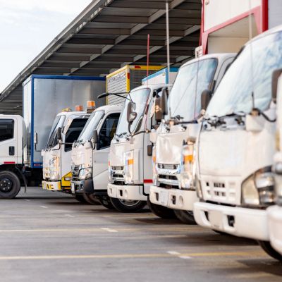 A row of white delivery trucks parked in a line under a covered area.
