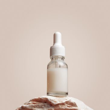 Dropper bottle filled with white liquid on a textured surface.