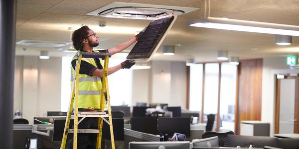 Ventilation engineer installing a ceiling air-conditioning vent.