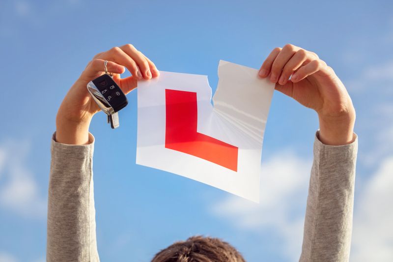 Tearing L plate against a sky holding a car key after passing driving test