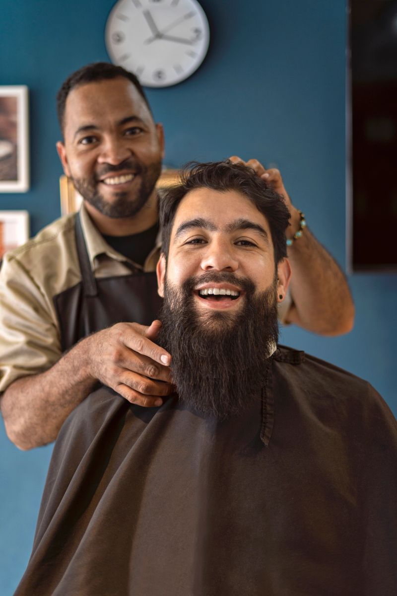 Portrait of an African American barber and a smiling customer looking at the camera in the barber shop for a haircut.