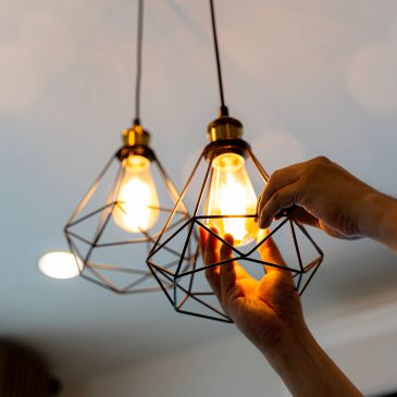 Hands adjusting a lit modern pendant light bulb fixture.