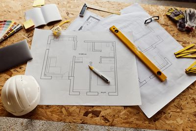 An architectural blueprint with measuring tools and a hard hat on a wooden table.
