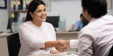 Two business people shaking hands across a meeting table in an Indian office