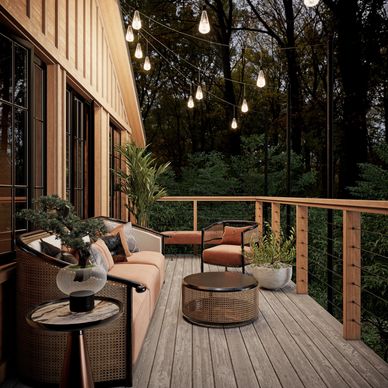 Cozy outdoor seating area on a wooden deck with string lights and lush greenery at dusk.