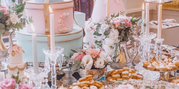 Elegant pastel-themed dessert table with flowers, candles, and cakes.