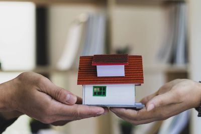 Two hands holding a small model house symbolizing real estate or home ownership.