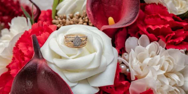 Engagement ring on a white rose surrounded by red and white flowers.