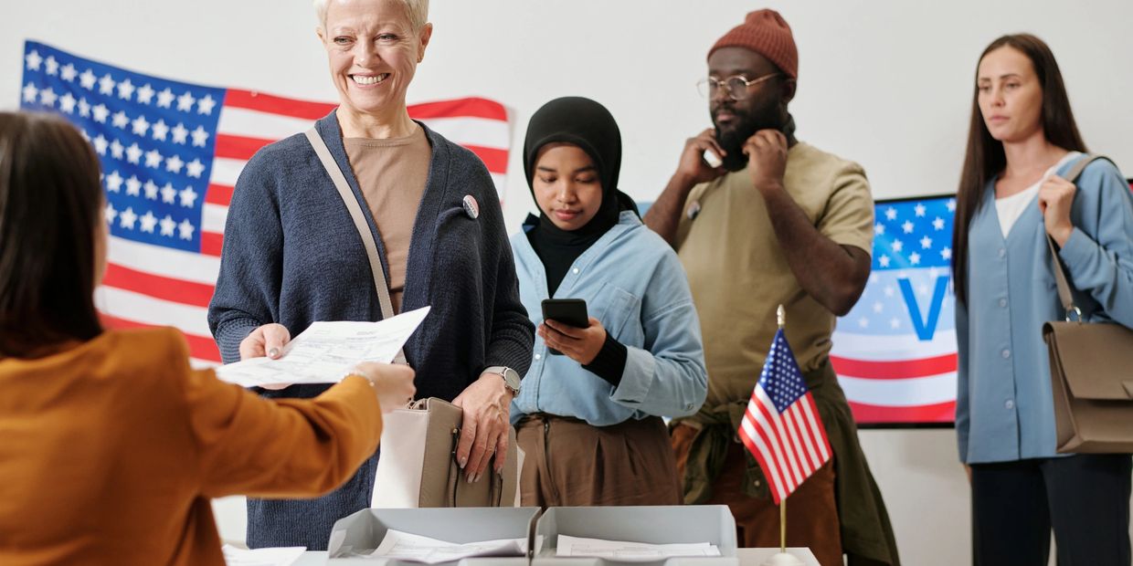 Diverse group of people at a US voting station with American flags.