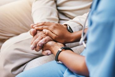 Healthcare worker holding an elderly person's hands in a comforting gesture.