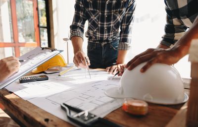 People reviewing architectural blueprints with a white safety helmet on the table.