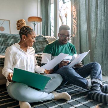 A couple sitting on the floor reviewing documents together in a cozy living room.