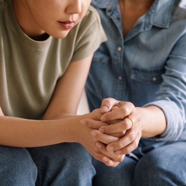 An adult therapist is holding a young woman's hand in support