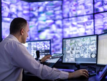 Man monitoring multiple surveillance screens in a control room.