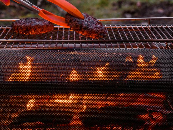 Grilling burger patties over an open flame with tongs.